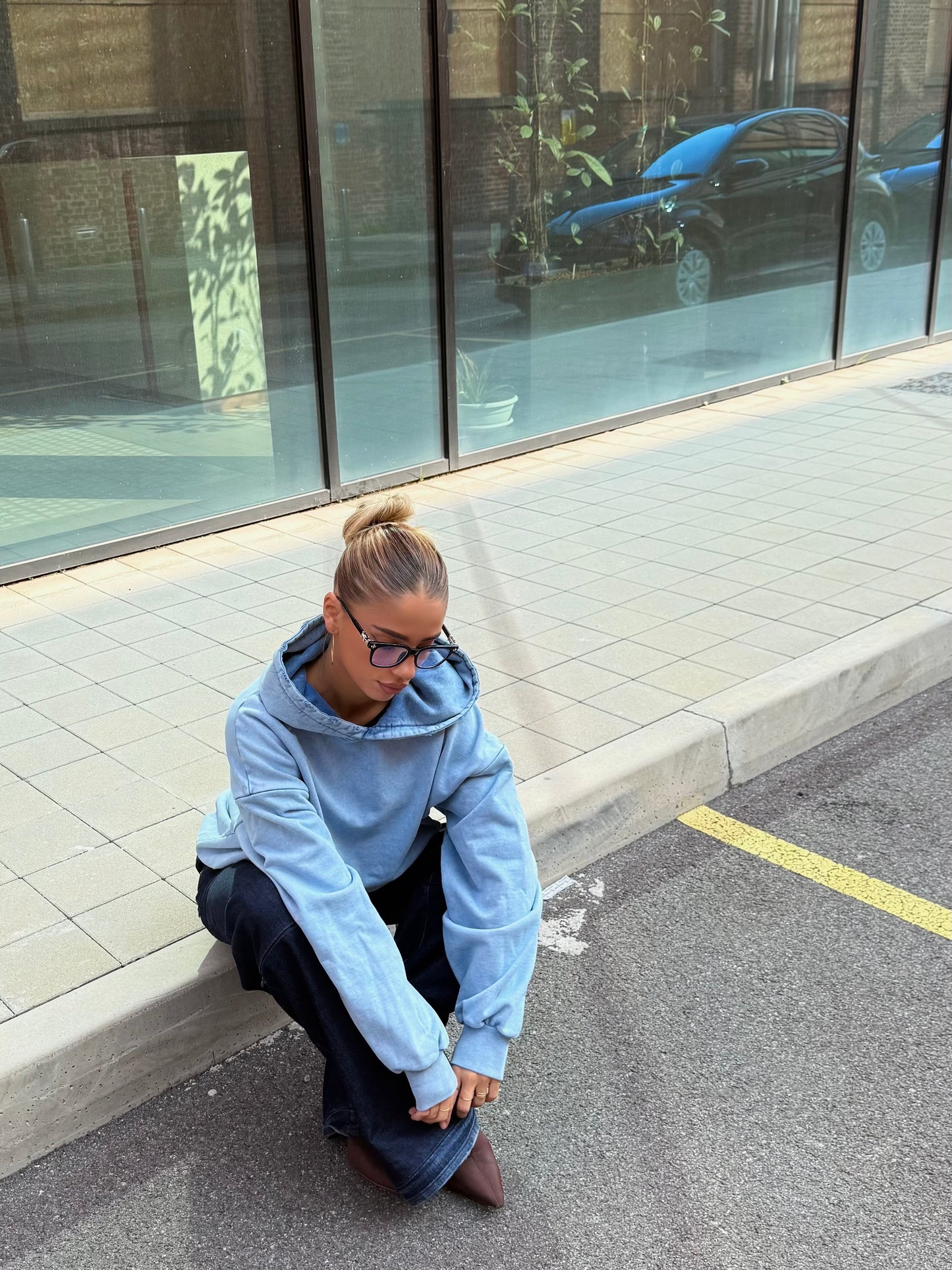 Donna seduta su marciapiede, indossa felpa azzurra e jeans modulari MO Interchangeable.