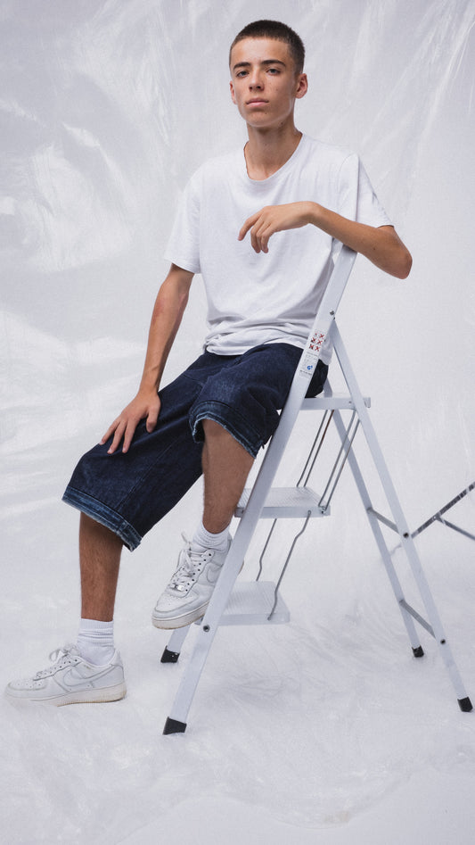 Ragazzo su scala indossa denim modulare MO Interchangeable e t-shirt bianca, sfondo neutro